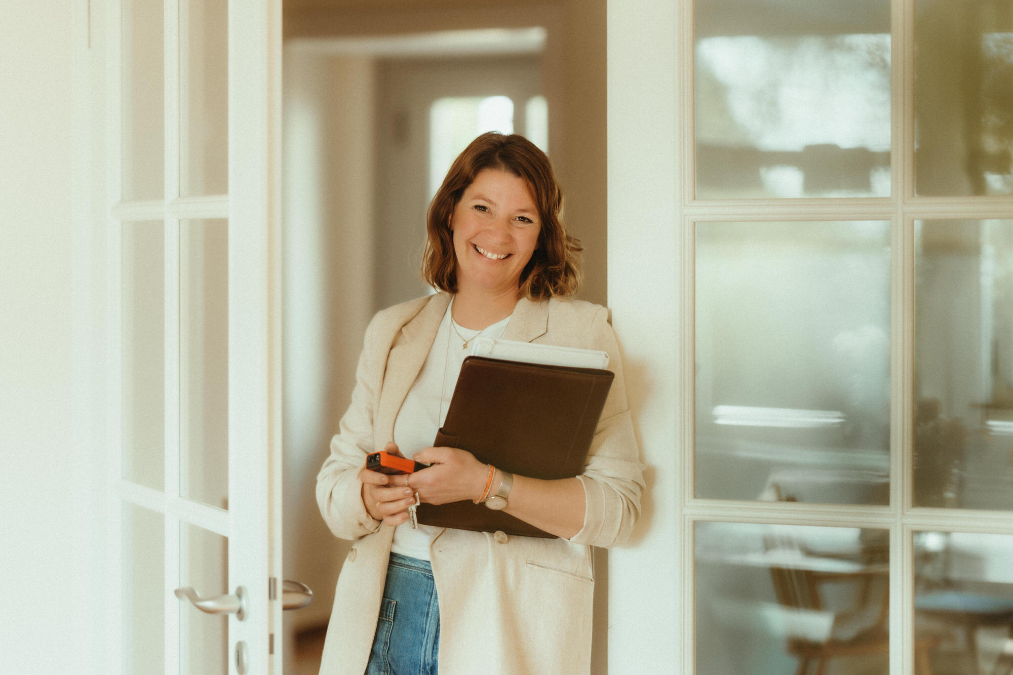 lächelnde Homestaging-Expertin mit Ordner und Maßband in einem hellen Raum